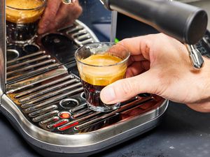 Hand holding freshly brewed espresso coffee on Breville Bambino Plus Espresso Machine tray