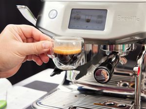 A person holding up a shot of espresso that was brewed from the Breville Barista Touch Impress Espresso Machine with Grinder