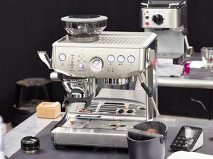 A Breville espresso machine on a countertop, with a knockbox and a tamper beside it.