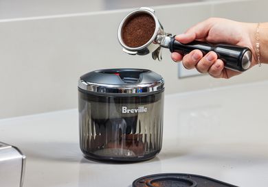 A person about to place a portafilter with espresso grounds in it into the Breville Puck Sucker.