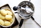 a food mill with boiled potatoes in a steamer basket on a white tile surface