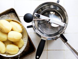 a food mill with boiled potatoes in a steamer basket on a white tile surface