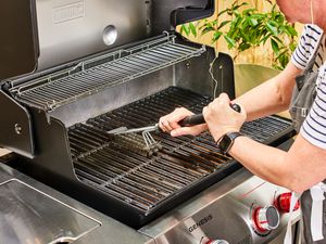 A person uses a grill brush to clean the Weber Genesis E-335 Gas Grill