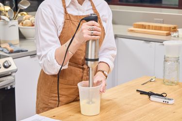 A person uses the All-Clad Stainless Steel Immersion Blender in a plastic container