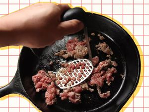 Smashing meat in a cast-iron skillet with a potato masher.