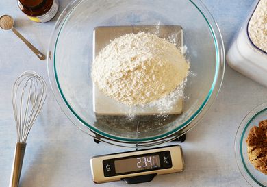 A glass bowl with flour on it set on a kitchen scale that has a pull-out screen.