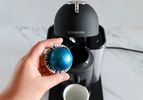 A hand holding an espresso pod in front of the Nespresso Vertuo Coffee and Espresso Machine by Breville