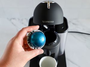 A hand holding an espresso pod in front of the Nespresso Vertuo Coffee and Espresso Machine by Breville