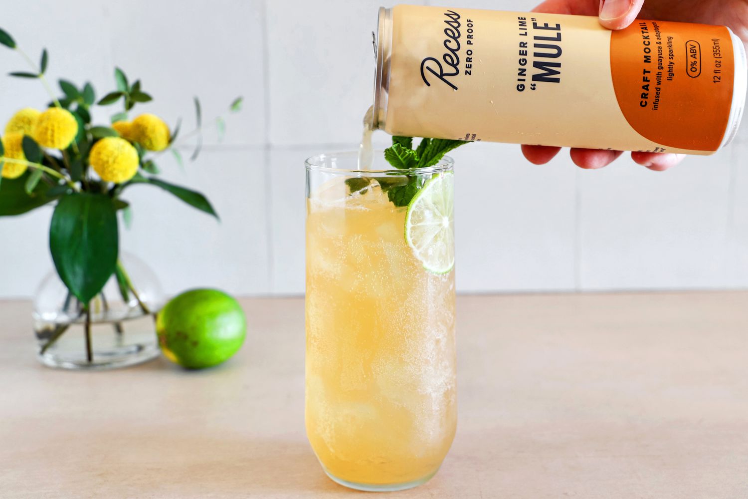 A person pouring a canned mocktail into a glass with ice.