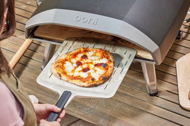 A person removing a pizza from the Ooni Koda 16 Gas Pizza Oven