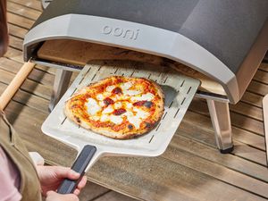 A person removing a pizza from the Ooni Koda 16 Gas Pizza Oven