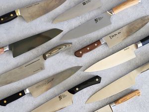 a variety of carbon steel chef's knives on a gray surface