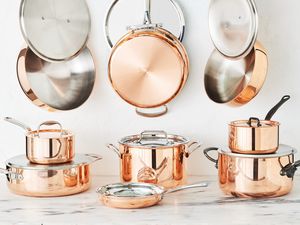 Several pieces of copper cookware on a marble kitchen countertop.