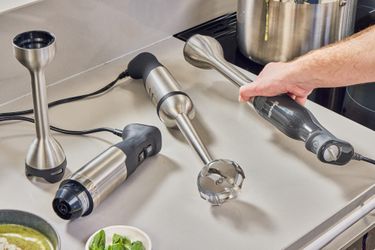 A number of immersion blenders on a kitchen countertop./