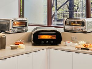 Three indoor pizza ovens on a kitchen countertop.