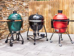 Three kamado grills on a stone patio