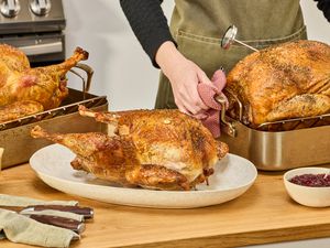 Three cooked turkeys on a kitchen countertop. A person is placing a turkey in a roasting pan onto the countertop.