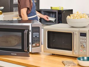 three microwaves on a wooden surface with a bowl of popcorn on top of one of them