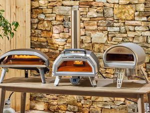 Three outdoor pizza ovens on a wooden table.