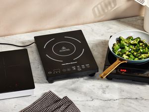 Three portable induction cooktops sit on a marble countertop. 