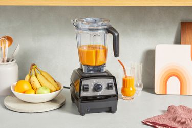 The Vitamix Propel 510 blender sits on a counter next to a fruit bowl and a glass of juice.