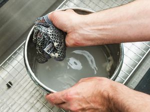 a hand using dough cloth to clean bread dough out of a bowl in a kitchen sink