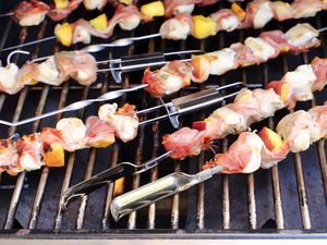 numerous skewers cooking on a gas grill