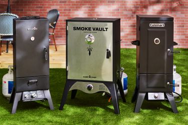 Three propane smokers sit side-by-side in a backyard.