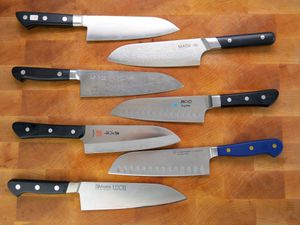 a variety of santoku knives on a wooden cutting board