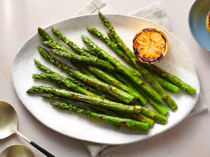 grilled asparagus served on a large serving plate, drizzled with olive oil, with lemon squeezed over the top, and garnished with charred lemons