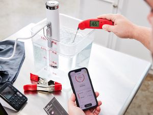 Person testing temperature of water in a bucket with the Breville Joule Sous Vide