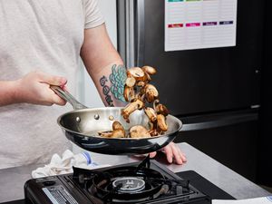 a person tossing mushrooms in a stainless steel skillet