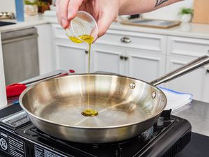 a hand pouring oil into a stainless steel skillet