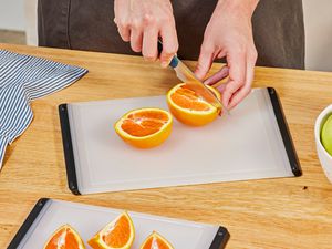 A person slicing an orange on the OXO plastic cutting board.