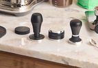 Three espresso tampers on a marble kitchen countertop.