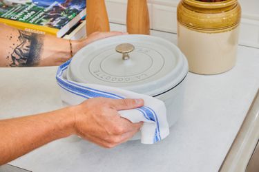 A person holding onto a Dutch oven's handles with a kitchen towel and placing it onto a countertop.