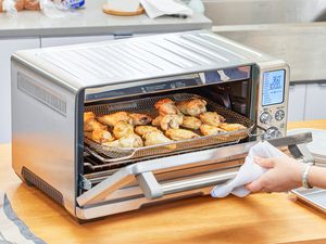 A hand opening the door to chicken cooking in the Breville the Smart Oven Air Fryer