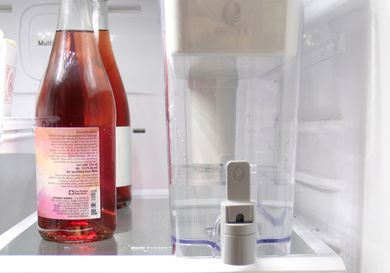 a water dispenser next to a few bottles of wine in the fridge