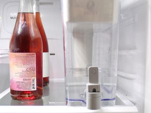 a water dispenser next to a few bottles of wine in the fridge