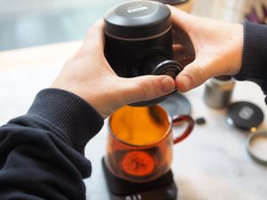 person adding topping to drink in orange glass mug