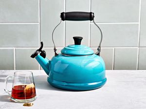 a blue tea kettle on a marble surface with a mug of tea beside it