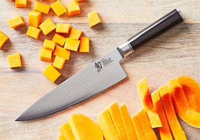 a closeup of the shun chef's knife on a wooden surface with cut up butternut squash