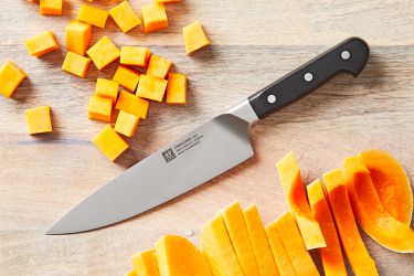 A chef's knife on a wooden surface with pieces of chopped squash beside it.