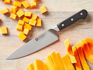 A chef's knife on a wooden surface with pieces of chopped squash beside it.