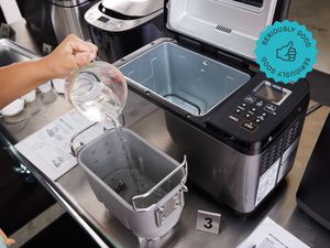 the zojirushi bread maker with someone putting water into the bread pan