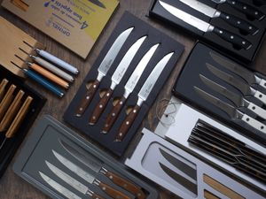 a variety of steak knives in their boxes on a wooden surface