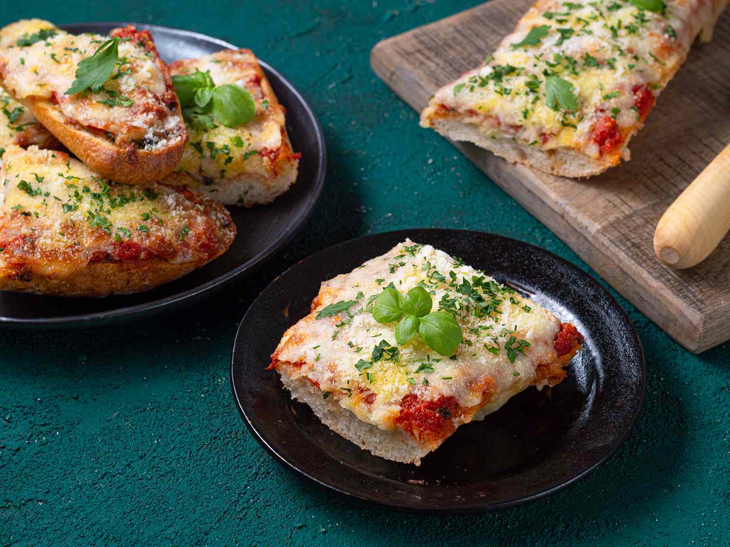 French bread pizza cut up and displayed on two ceramic plates and on a wooden cutting board.