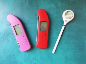 One white, one red, and one pick thermometer on a blue surface