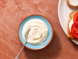 Two-minute mayonnaise in a serving bowl with a spoon, with an open face tomato sandwich on the right edge of the frame.