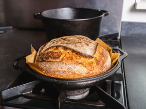 A round bread loaf in a parchment paper sling sitting in the shallow base of a cast iron combo cooker